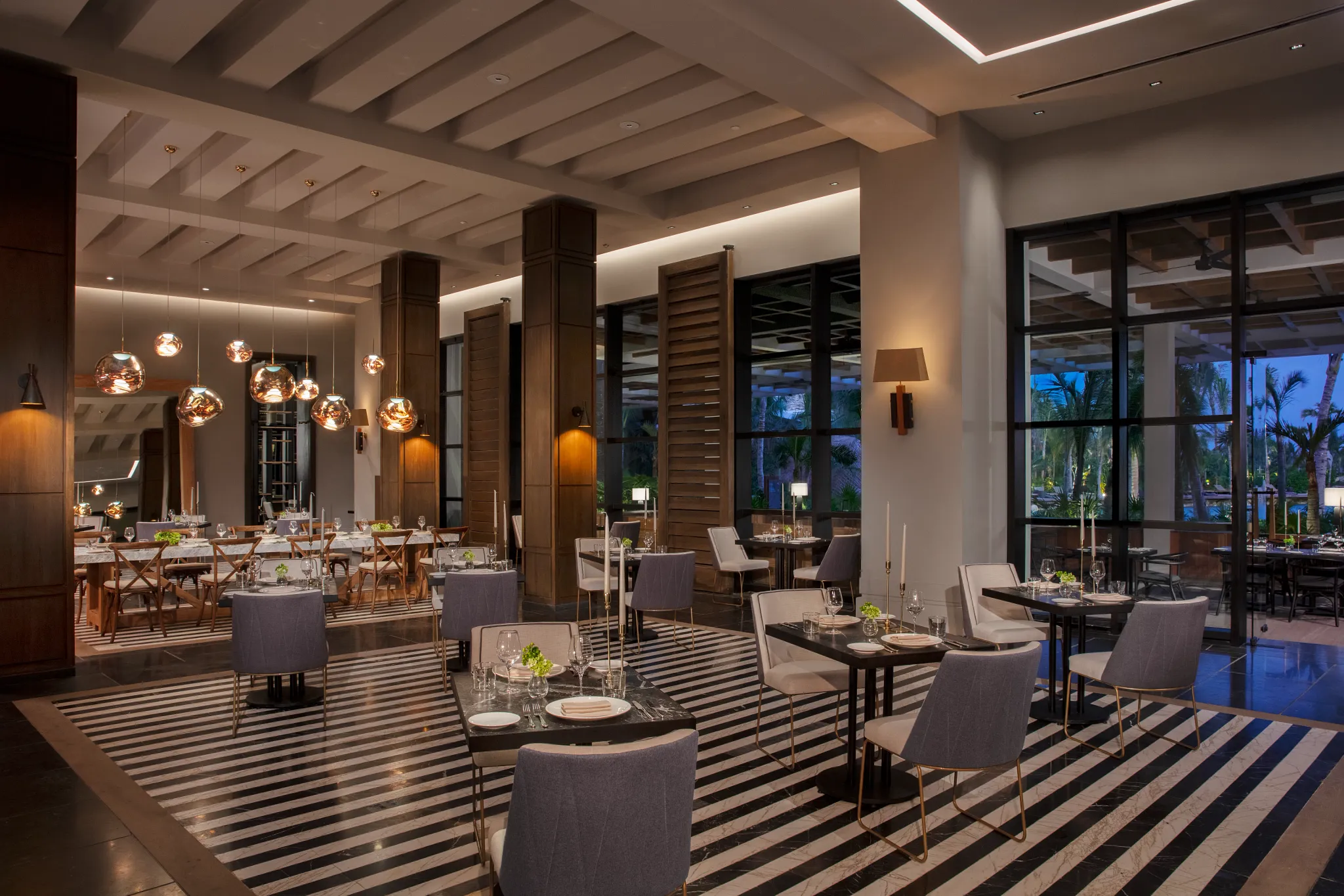 Allora Italian restaurant at Impression Moxché by Secrets featuring elegant modern dining, warm pendant lighting, floor-to-ceiling windows, and refined table settings.