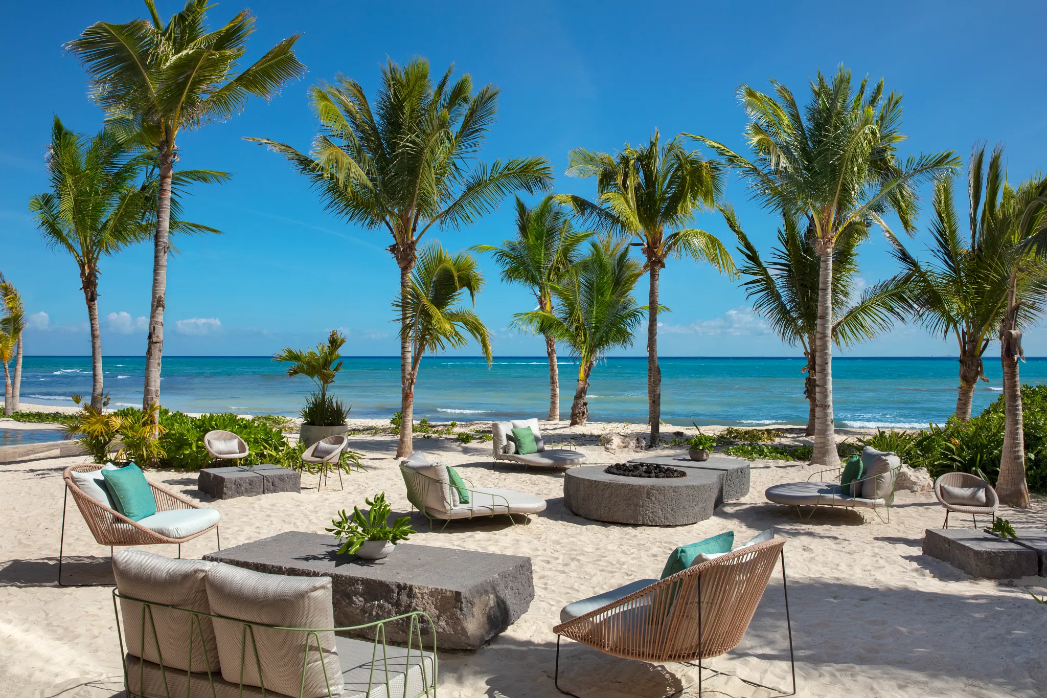 Modern lounge seating on the beach surrounded by palm trees at Impression Moxché by Secrets.